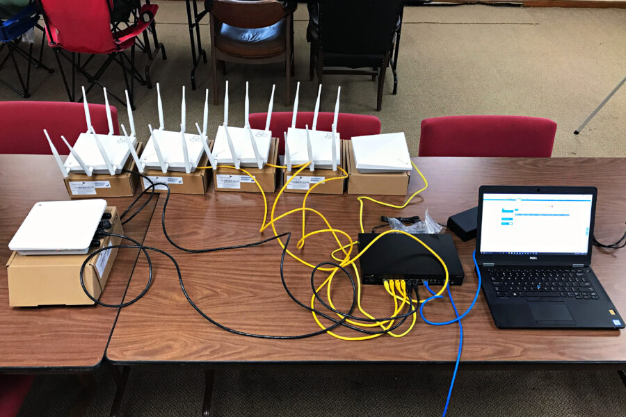 Multiple wireless access points connected with ethernet cables to a network switch. Laptop on the right, ABS Technology is configuring up the network equipment on the laptop.