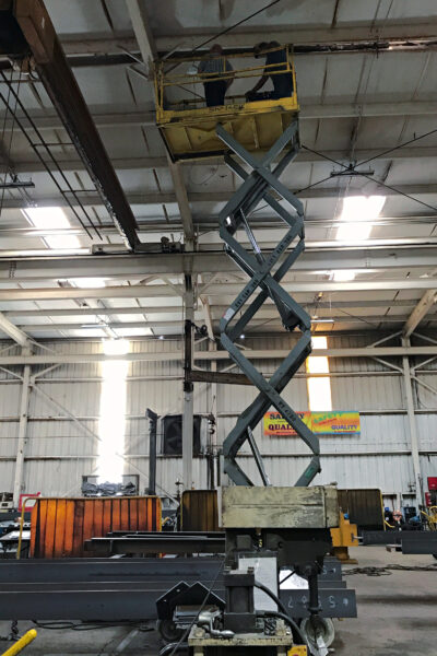 ABST Technicians on an elevated scissor lift inside a warehouse, working near the ceiling to install network equipment.